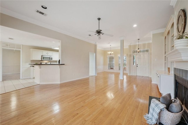 living room featuring a tile fireplace, ceiling fan with notable chandelier, light hardwood / wood-style flooring, and crown molding