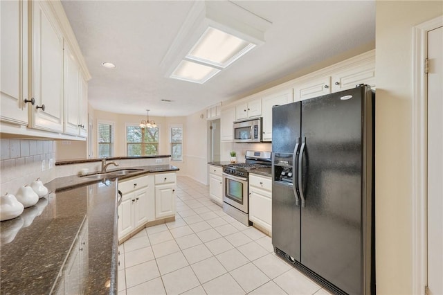 kitchen featuring sink, a notable chandelier, dark stone counters, decorative light fixtures, and appliances with stainless steel finishes