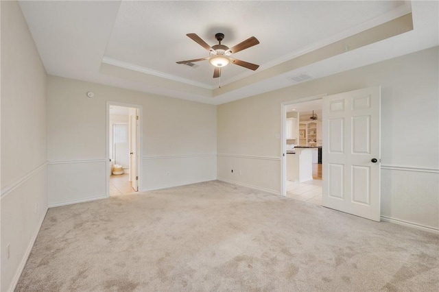 spare room with ceiling fan, a raised ceiling, light colored carpet, and ornamental molding