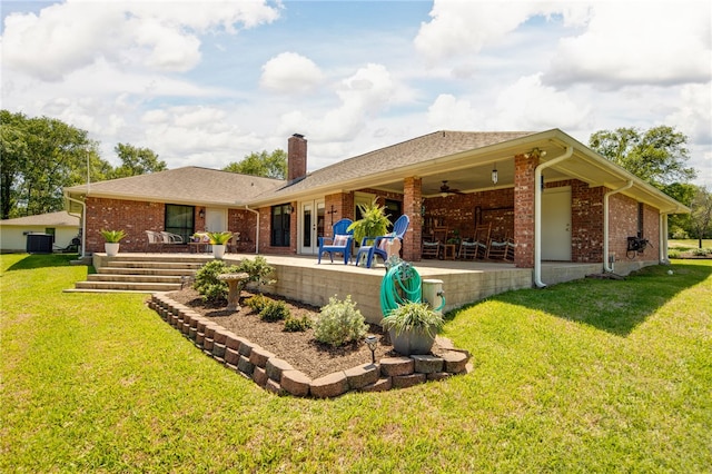 back of property featuring a ceiling fan, a chimney, a yard, and brick siding
