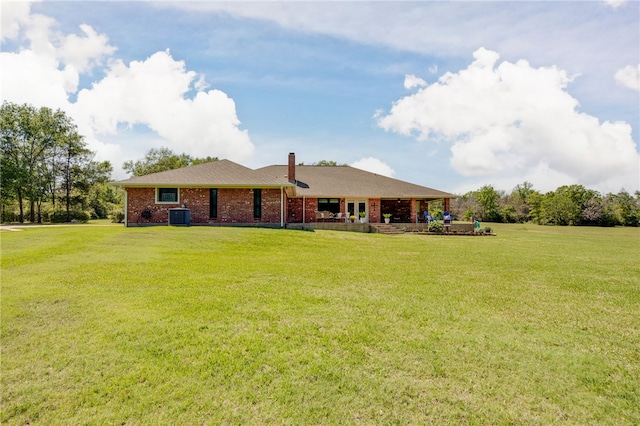 back of house featuring central air condition unit, a lawn, a chimney, and brick siding