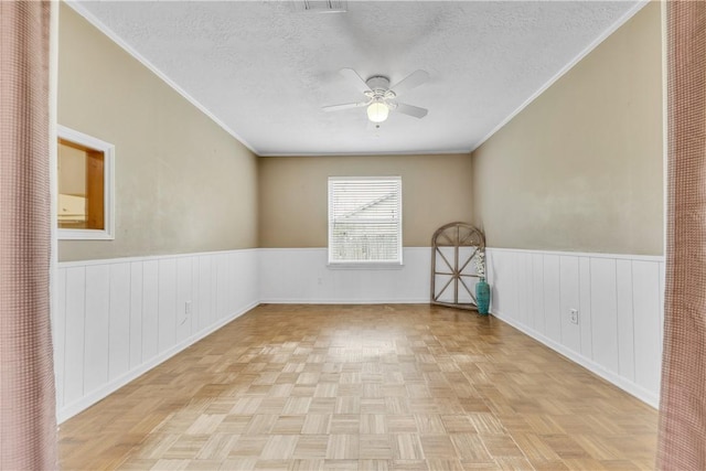 empty room featuring ceiling fan, ornamental molding, a textured ceiling, and light parquet flooring