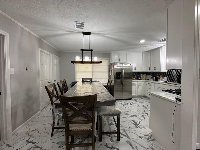 1906 Calvert Cir, Bryan, TX 77803 - kitchen with stainless steel fridge with ice dispenser, light marble finish floors, white cabinetry, ornamental molding, and a chandelier