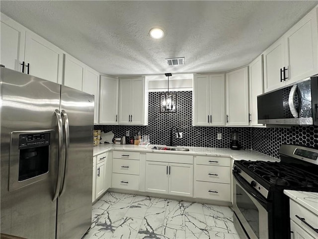 1906 Calvert Cir, Bryan, TX 77803 - kitchen featuring appliances with stainless steel finishes, a textured ceiling, light marble finish flooring, light countertops, and white cabinetry