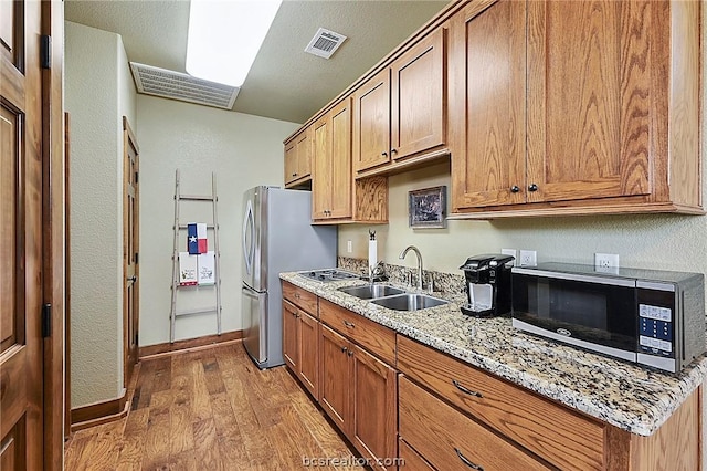 kitchen with sink, light stone counters, light hardwood / wood-style flooring, a textured ceiling, and appliances with stainless steel finishes