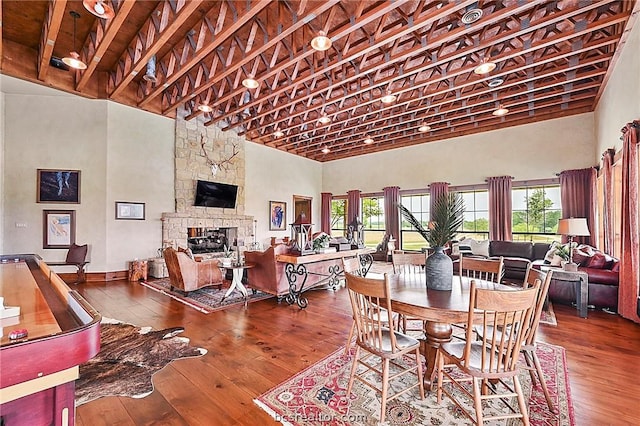 dining space featuring hardwood / wood-style flooring, a stone fireplace, and high vaulted ceiling