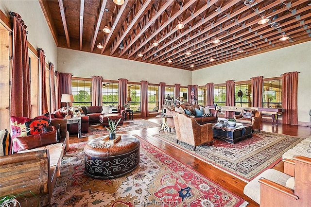 living room featuring beam ceiling, rail lighting, a towering ceiling, and hardwood / wood-style flooring