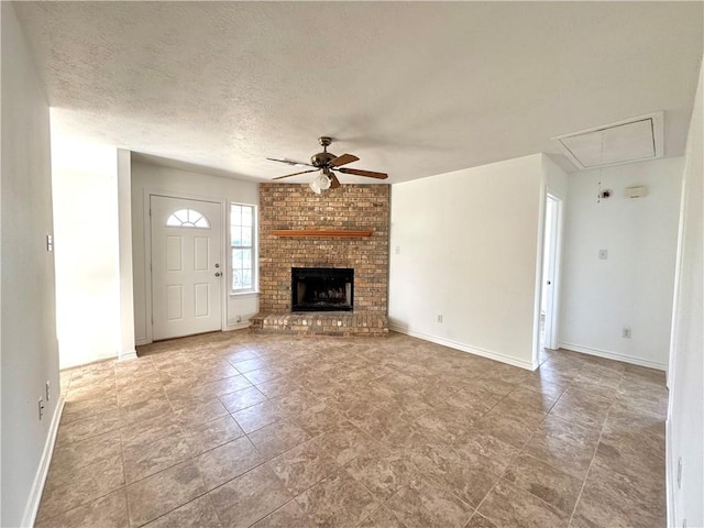 unfurnished living room with attic access, baseboards, a ceiling fan, a textured ceiling, and a brick fireplace