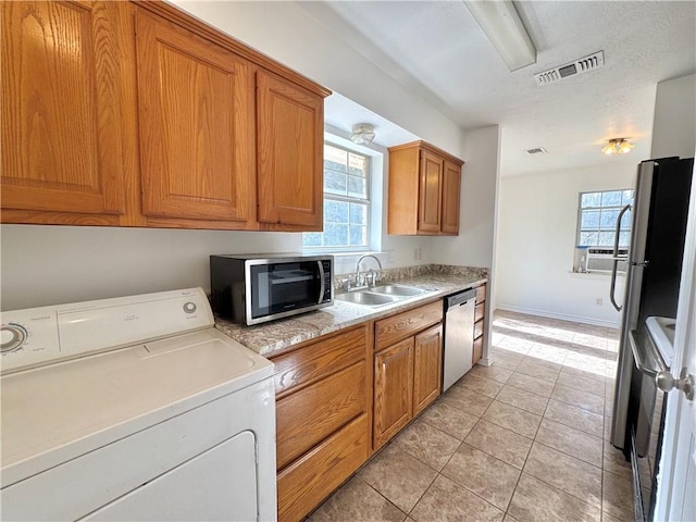 kitchen featuring stainless steel appliances, a sink, visible vents, brown cabinetry, and washer / dryer