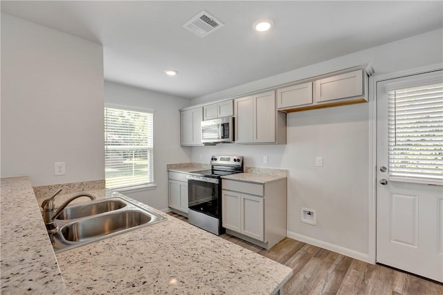 kitchen with light stone counters, sink, stainless steel appliances, and light hardwood / wood-style floors