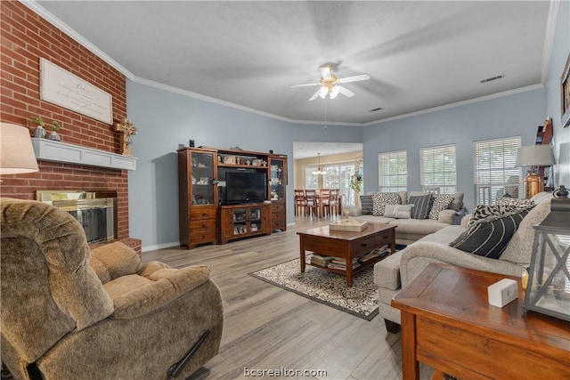 living room featuring a brick fireplace, ceiling fan with notable chandelier, crown molding, and light hardwood / wood-style flooring