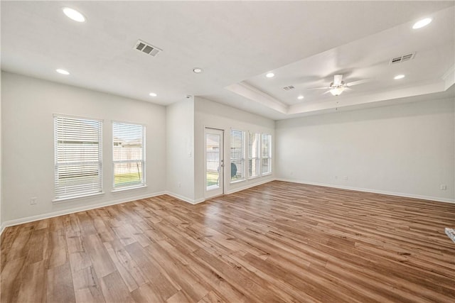 unfurnished living room with ceiling fan, a tray ceiling, and light hardwood / wood-style flooring