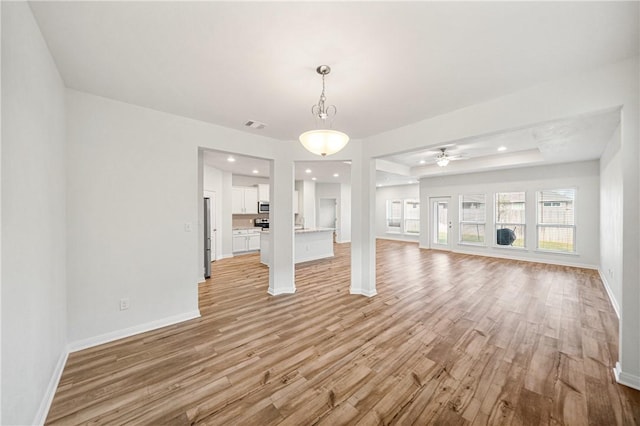 unfurnished living room featuring light wood-type flooring, a tray ceiling, and ceiling fan