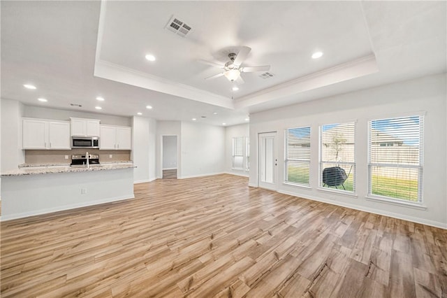 unfurnished living room featuring a raised ceiling, ceiling fan, light hardwood / wood-style flooring, and ornamental molding