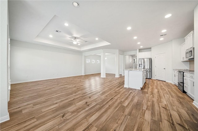 unfurnished living room featuring ceiling fan, light hardwood / wood-style floors, a raised ceiling, and sink