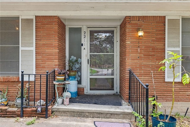 entrance to property with fence, a porch, and brick siding