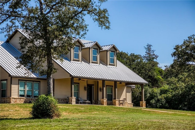 view of front of property with a front yard, a standing seam roof, metal roof, ceiling fan, and stone siding