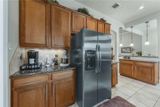 kitchen with decorative light fixtures, tasteful backsplash, stainless steel fridge, dark stone counters, and light tile patterned floors