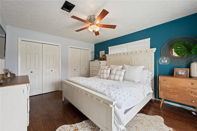 bedroom with multiple closets, ceiling fan, dark wood-style floors, and visible vents