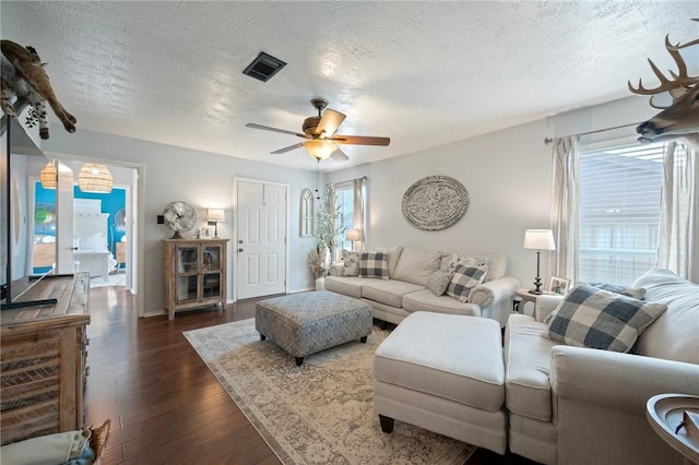 living area with a ceiling fan, a textured ceiling, visible vents, dark wood finished floors, and baseboards