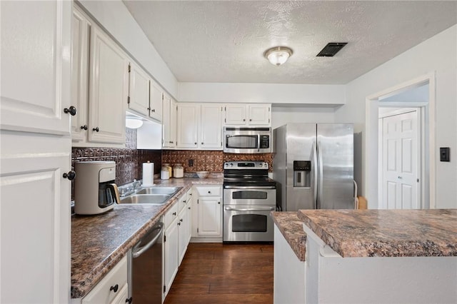 kitchen featuring visible vents, dark countertops, dark wood-style floors, a sink, and stainless steel appliances