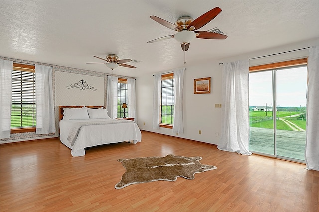 unfurnished bedroom with access to exterior, multiple windows, a textured ceiling, and wood finished floors