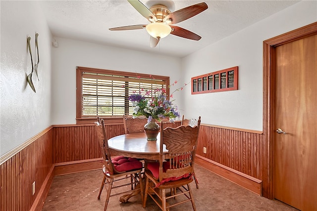 dining area with wainscoting, ceiling fan, wooden walls, and a textured ceiling