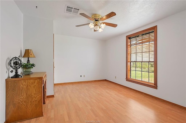 spare room with light wood finished floors, visible vents, baseboards, ceiling fan, and a textured ceiling