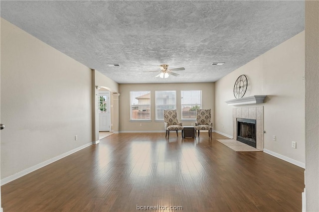 unfurnished living room with ceiling fan, dark hardwood / wood-style flooring, a textured ceiling, and a tile fireplace