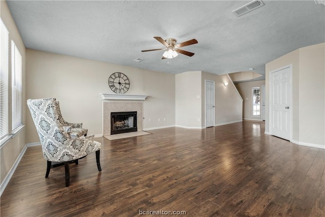 living area featuring a textured ceiling, a tiled fireplace, a wealth of natural light, and dark hardwood / wood-style floors