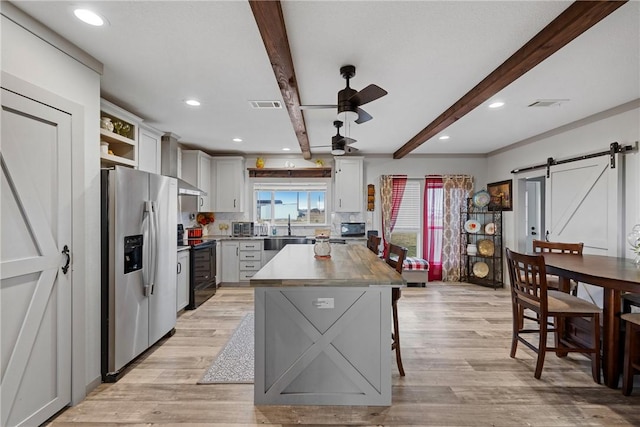 kitchen featuring stainless steel refrigerator with ice dispenser, visible vents, a barn door, a kitchen island, and black / electric stove