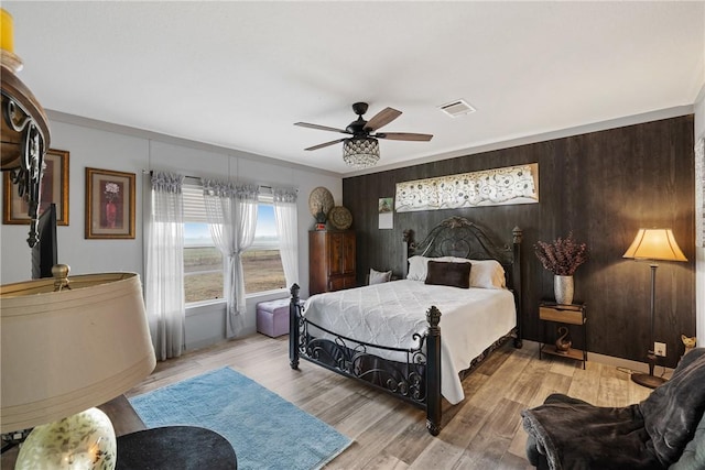 bedroom featuring light wood finished floors, wooden walls, visible vents, and a ceiling fan