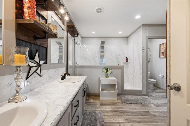 full bathroom with double vanity, toilet, wood finished floors, a shower stall, and a sink