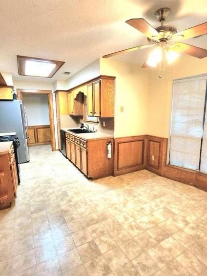 1706 Shawnee St, Navasota, TX 77868 - kitchen with brown cabinets, a wainscoted wall, light countertops, a sink, and appliances with stainless steel finishes