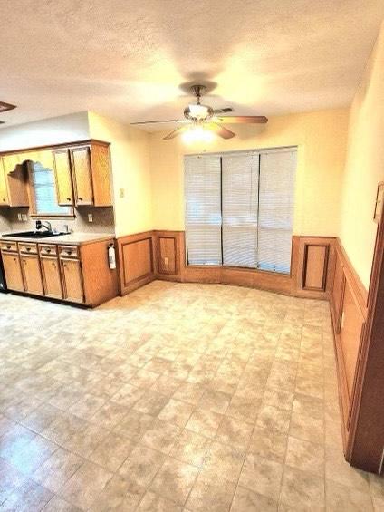 1706 Shawnee St, Navasota, TX 77868 - kitchen featuring brown cabinets, ceiling fan, a wainscoted wall, a textured ceiling, and a decorative wall
