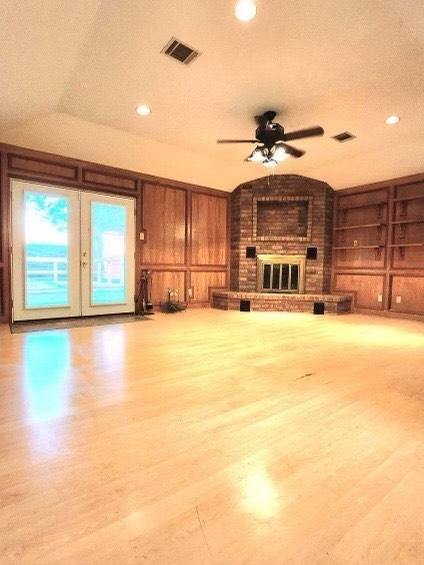 1706 Shawnee St, Navasota, TX 77868 - unfurnished living room featuring a fireplace, built in features, a ceiling fan, wood finished floors, and wooden walls