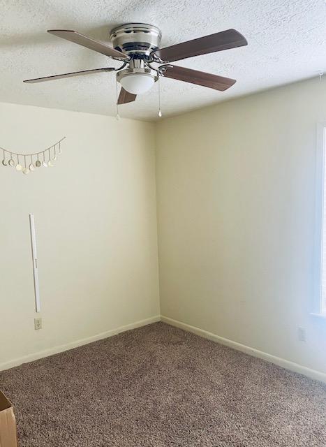 carpeted spare room featuring a textured ceiling, ceiling fan, and baseboards