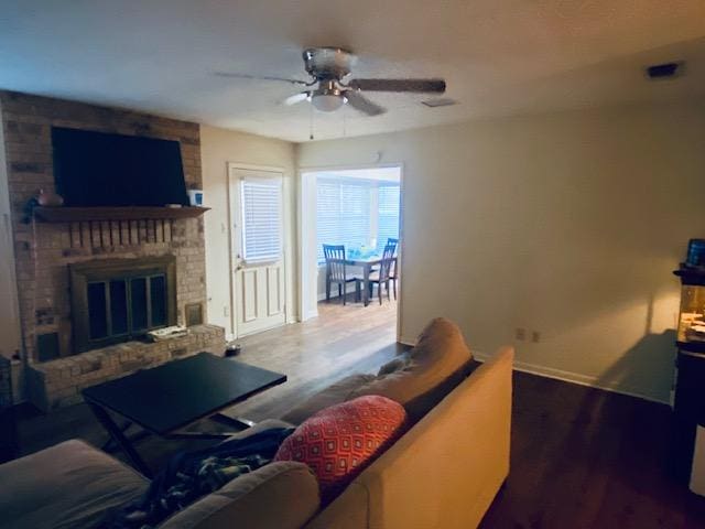 living room featuring ceiling fan, visible vents, a fireplace, and wood finished floors