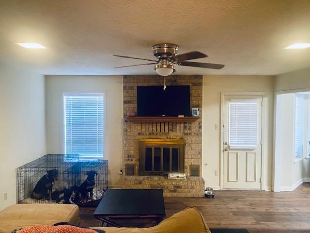 living room with a textured ceiling, ceiling fan, a fireplace, wood finished floors, and visible vents