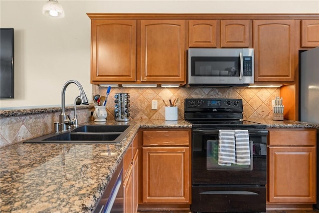 kitchen featuring stainless steel appliances, a sink, dark stone counters, decorative backsplash, and brown cabinetry