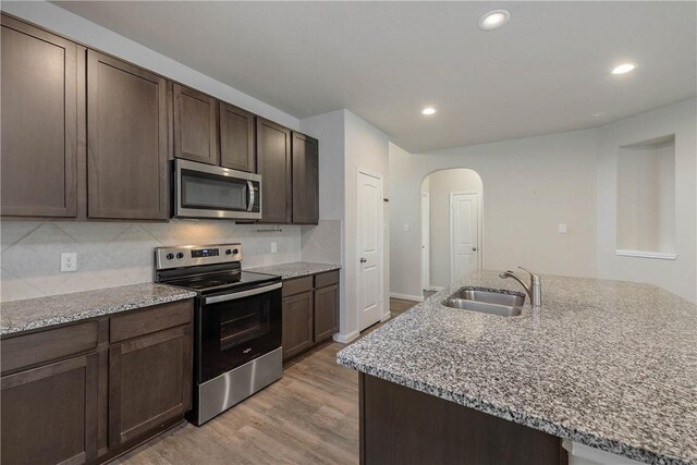 4706 Coyotillo Way, Bryan, TX 77807 - kitchen with stainless steel appliances, arched walkways, light wood-style flooring, light stone counters, and dark brown cabinets