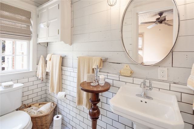 half bath featuring ceiling fan, toilet, wood walls, and a sink