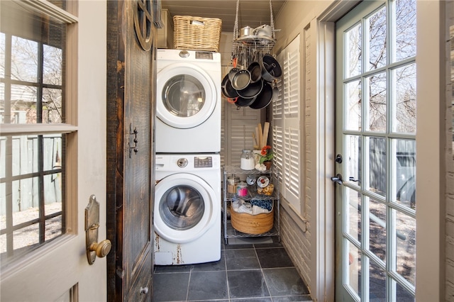 washroom with a wealth of natural light, dark tile patterned flooring, laundry area, and stacked washer / dryer