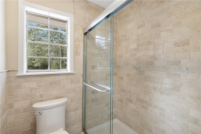 bathroom with toilet, a shower with door, and tile walls