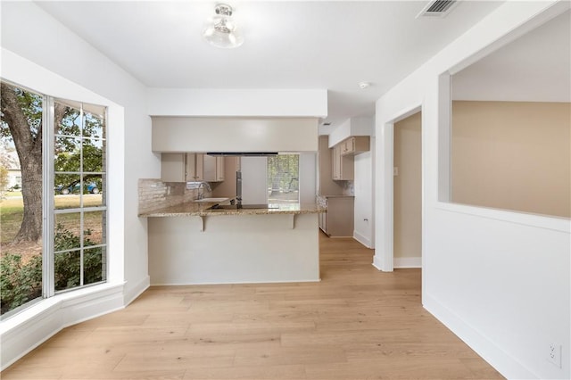 kitchen featuring light hardwood / wood-style floors, light stone counters, kitchen peninsula, and sink