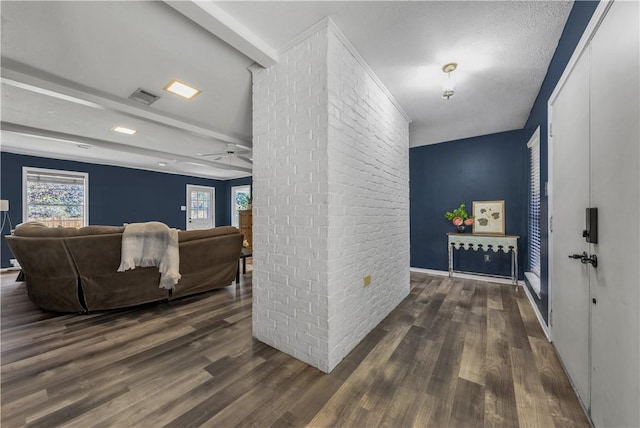 corridor featuring beamed ceiling, a textured ceiling, dark hardwood / wood-style flooring, and brick wall