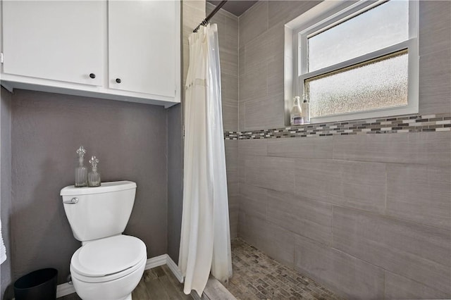 full bathroom featuring toilet, wood finished floors, baseboards, and tiled shower