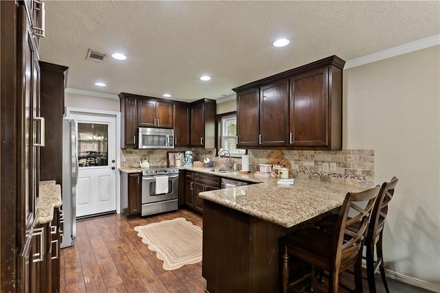 kitchen with stainless steel appliances, visible vents, crown molding, dark brown cabinetry, and a peninsula