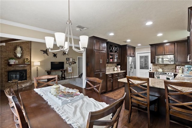 dining area featuring an inviting chandelier, crown molding, dark wood-type flooring, and a fireplace