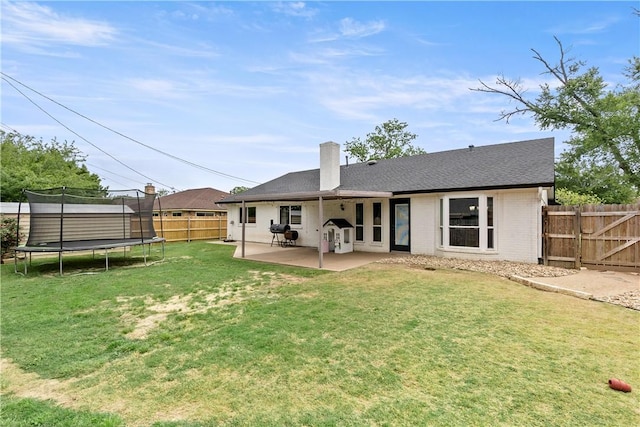 rear view of house featuring a fenced backyard, a patio, a lawn, brick siding, and a trampoline